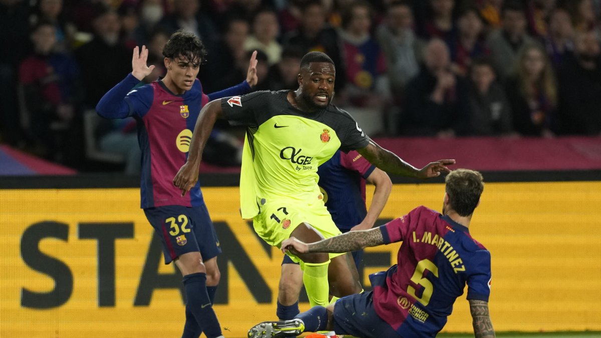 El delantero del Mallorca Cyle Larin (c) juega un balón entre Héctor Fort (i) e Íñigo Martínez, ambos del Barcelona, durante el partido de la jornada 33 de LaLiga que FC Barcelona y RCD Mallorca disputaron en el Estadi Olímpic Lluís Companys. EFE/Alejandro García