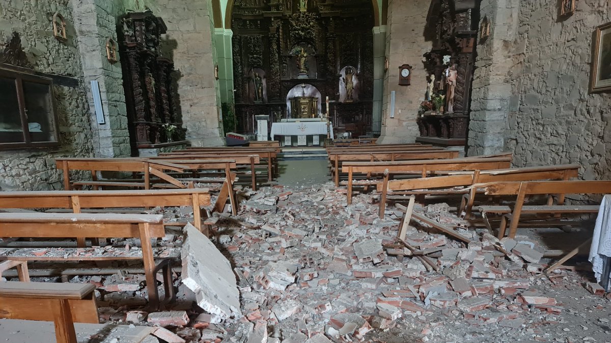 Trozos de ladrillo y escayola desprendidos sobre la fila de bancos y el pasillo de la nave.