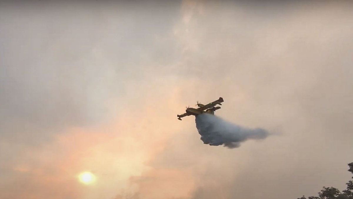 Un hidroavión descarga agua mientras efectivos de la UME realizan trabajos de liquidación de reproducción en la zona de Galende, en el incendio forestal de Porto (Zamora). EFE/Ministerio de Defensa )
