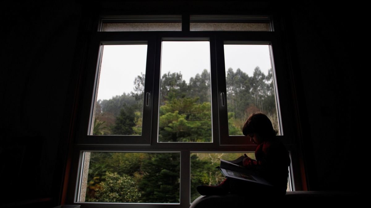 Un niño en libro al lado de la ventana.