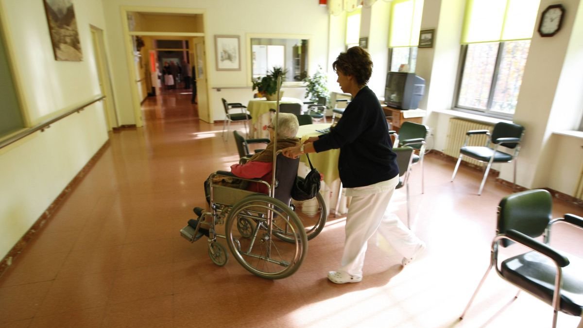 Una trabajadora traslada a una persona mayor en silla de ruedas.