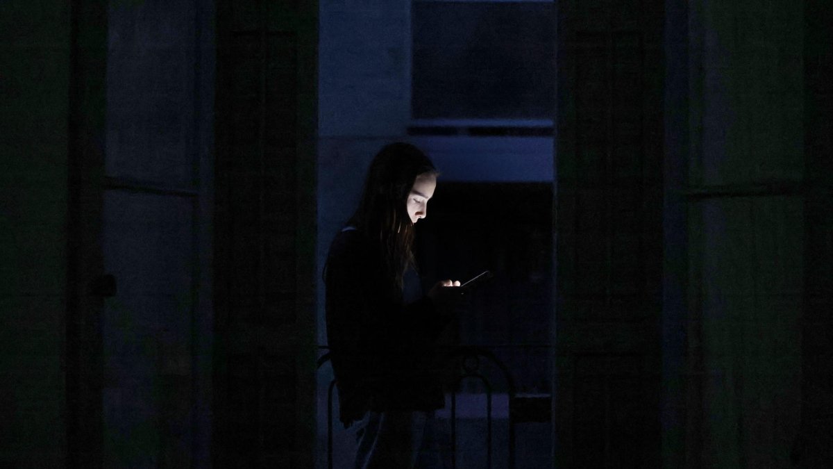 Un joven consulta su teléfono móvil en un balcón de Barcelona durante el apagón. EFE/Alberto Estévez.