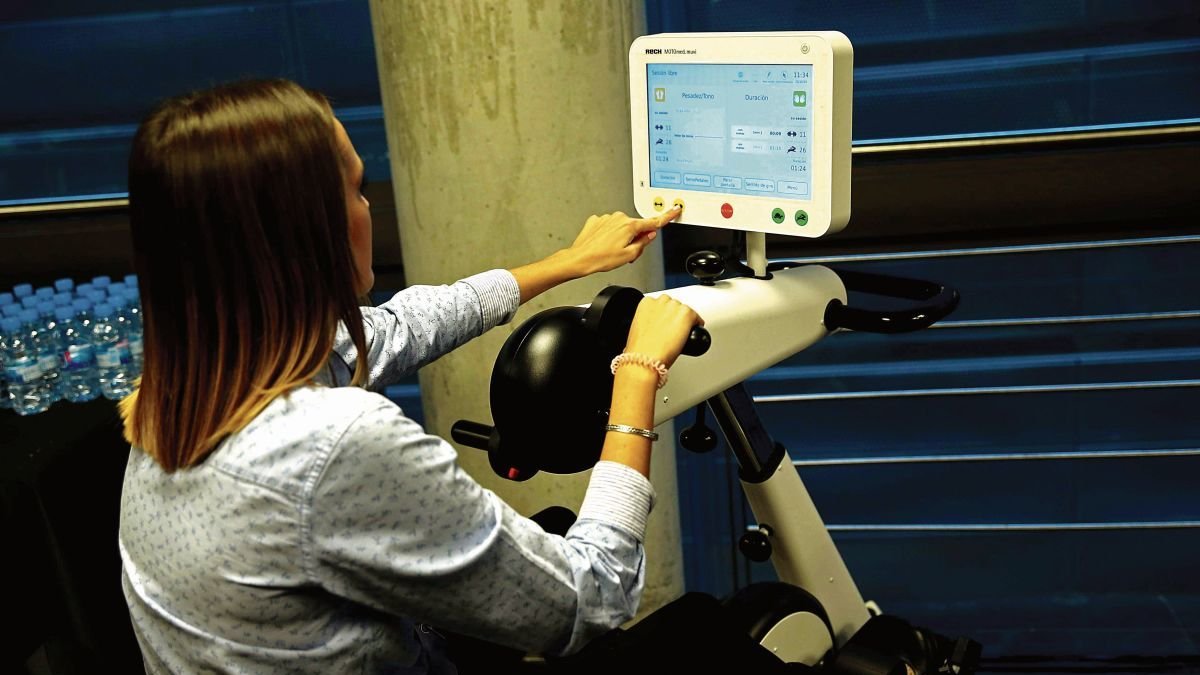 Una mujer muestra una máquina que se usa en la rehabilitación motora del ictus.