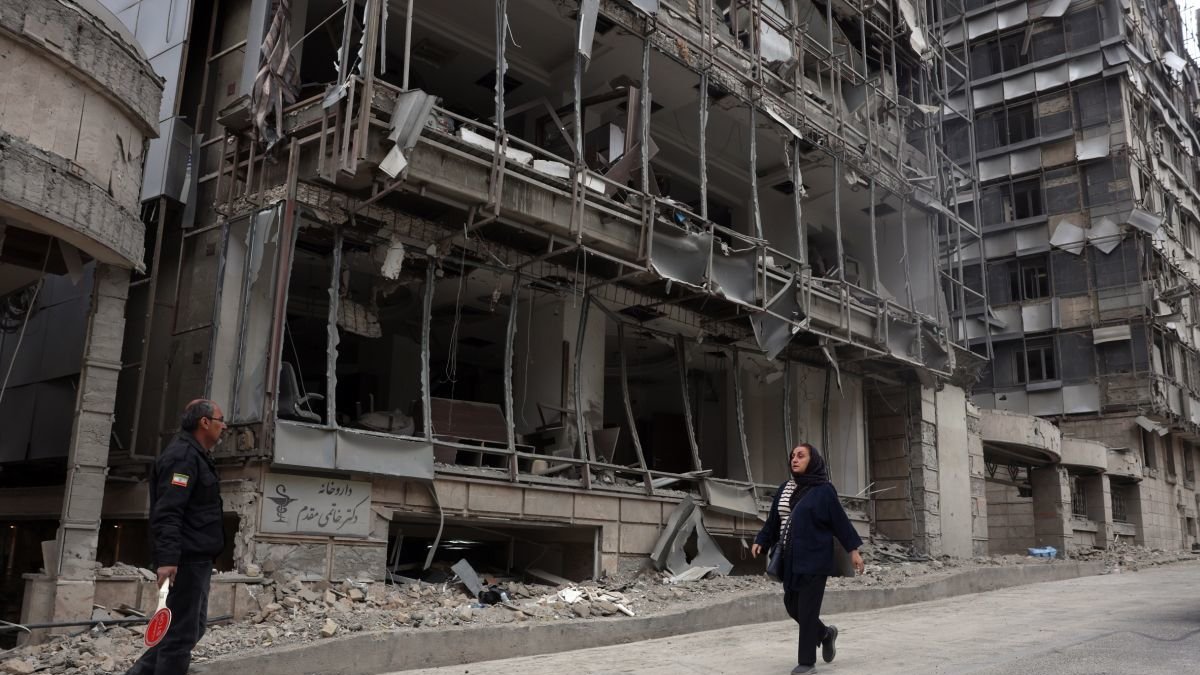 Dos iraníes pasan delante de un edificio bombardeado.