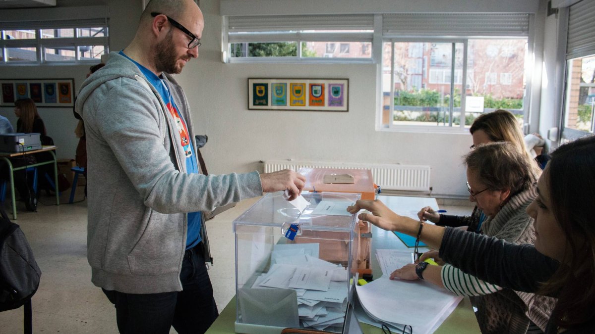 Un ciudadano introduce su voto en la urna ante la supervisión de los miembros de la mesa durante una jornada electoral en un colegio electoral.