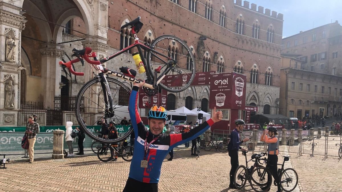 Alberto Viejo Escudero 'Albertín' levanta su bicicleta tras completar la Strade Bianche en 2023.