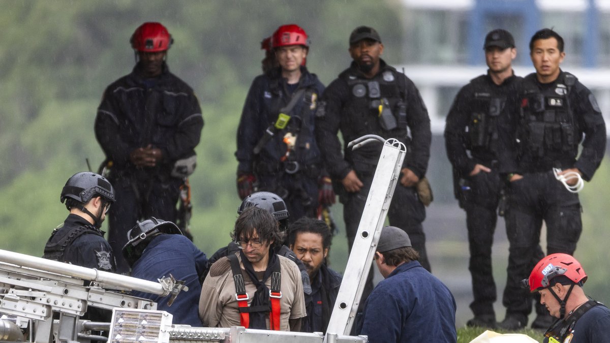 Un equipo de respuesta de emergencia desata al manifestante Guido Reichstadter (C) tras ayudarlo a bajar desde lo alto del puente Frederick Douglass Memorial Bridge en el sexto día de su protesta contra la guerra de Irán en Washington