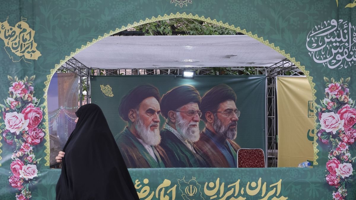 Una mujer pasa delante de un cartel en Teherán que muestra a los líderes de la República Islámica, incluido Mojtaba Jameneí.