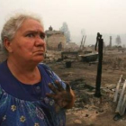Una mujer posa delante de los restos de su pueblo, asolado por los incendios.