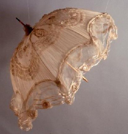Sombrilla con cubierta de ocho paños de gasa cruda y volante al aire de la misma gasa, con tres cintas de seda cruda aplicadas en sentido horizontal, cosidas a máquina, con 16 medallones encima de encaje y raso crudos. Obra entregada al Museo del Pueblo Español (hoy Museo del Traje. CIPE) en calidad de depósito por la Comisaría General del Servicio de Defensa del Patrimonio Artístico Nacional, el 6 de abril de 1943.