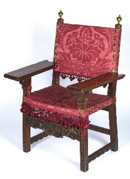 Silla de brazos con chambrana frontal tallada en bajorrelieve, brazos rectos muy anchos, remates en forma de bola de bronce dorado y tapizado al aire de respaldo y asiento de damasco de seda de color carmesí. Obra procedente de la colección de José Arnaldo Weissberger Kahn (1878-1954) incautada el 1 de junio de 1939 por la Comisaría General del Servicio de Defensa del Patrimonio Artístico Nacional y depositada en el Museo Nacional de Artes Decorativas.
