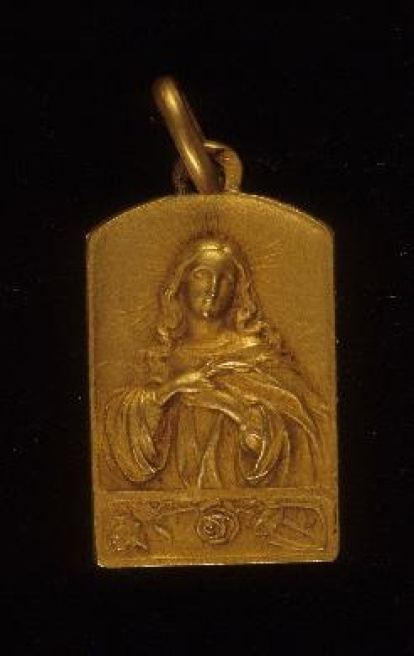 Medalla rectangular, la parte superior ligeramente curvada, con imagen de busto de la Virgen en relieve, y en la parte inferior del campo, en horizontal, una rama floreada. Tiene asa fija en la parte superior y otra móvil prendida a esta, para suspensión. El reverso es liso. Obra entregada en calidad de depósito por el Ministerio de Cultura al Museo del Pueblo Español, el 23 de septiembre de 1978 (en copia mecanografiada se transcribe erróneamente 1971). La obra se encontraba en el Casón del Buen Retiro, sede de los almacenes de la Comisaría del Patrimonio Artístico desde 1971.