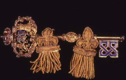Broche en forma de llave de gentilhombre, con corona real y, entre castillo y león rampante presenta el número XIII. Presenta cierre de bisagra, alfiler y seguridad. Obra entregada en calidad de depósito por el Ministerio de Cultura al Museo del Pueblo Español, el 23 de septiembre de 1978 (en copia mecanografiada se transcribe erróneamente 1971).