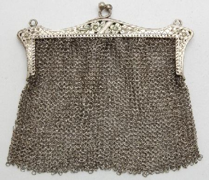 Bolsa plana de tendencia trapezoidal, realizada en tejido de malla. Boquilla rectangular de perfil mixtilíneo, decorada con calados y grabados vegetales y líneas en retícula; cierre de botón y asas para suspender la cadena. Obra entregada en calidad de depósito por el Ministerio de Cultura al Museo del Pueblo Español, el 23 de septiembre de 1978 (en copia mecanografiada se transcribe erróneamente 1971). La obra se encontraba en el Casón del Buen Retiro, sede de los almacenes de la Comisaría del Patrimonio Artístico desde 1971.