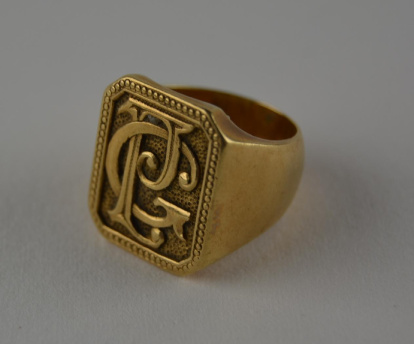 Anillo en oro amarillo, con aro ancho y plano, que remata en un sello de formato rectangular con los bordes en chaflán. El interior del aro es liso. El sello dispone de una cenefa continuada de puntos pequeños. El campo está ligeramente rehundido, con textura de puntos. Sobre este campo se localizan las letras P y G superpuestas, entrelazadas y estilizadas. Datado entre 1880 y 1936. Obra entregada en calidad de depósito por el Ministerio de Cultura al Museo Nacional de Cerámica, el 23 de septiembre de 1978.