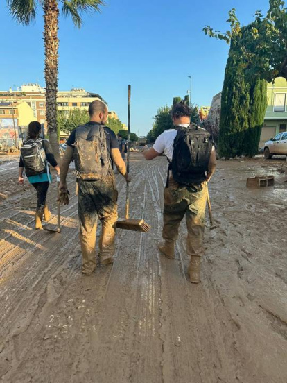 Voluntarios con escobones en medio de una calle llena de barro y lodo.