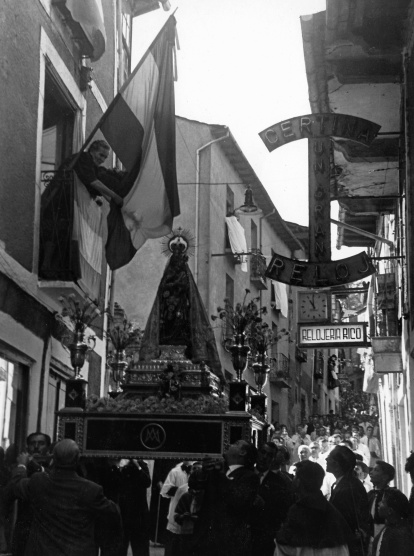 Doña Gregoria, esposa del maestro Don Vitaliano, desenreda la bandera nacional que se ha enganchado en la corona de la Virgen.